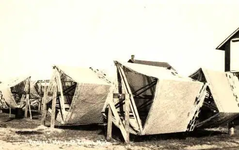 Row of canvas-covered wooden-frame structures beside a partially visible building.