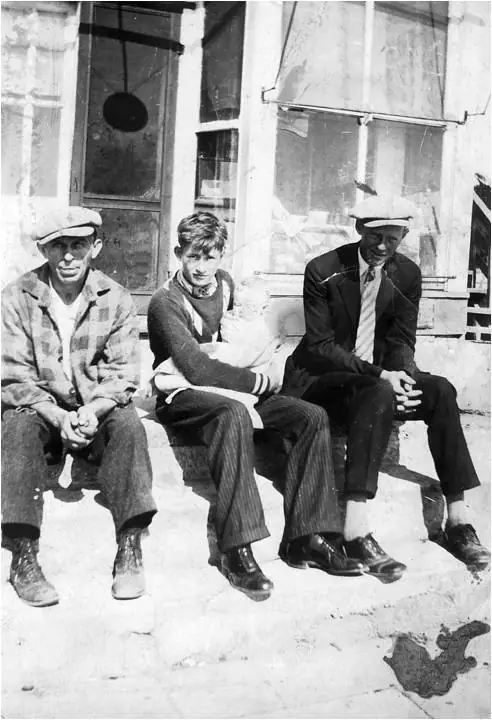 Three men in work and formal clothing sit outside a building with windows and a glass door.