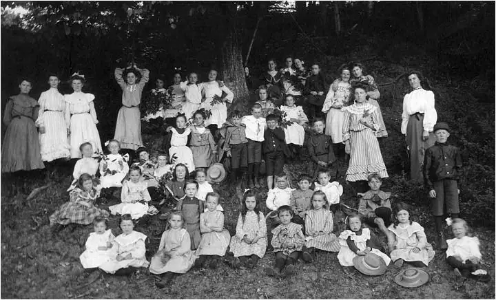 A large group of adults and children poses on a grassy, wooded slope.