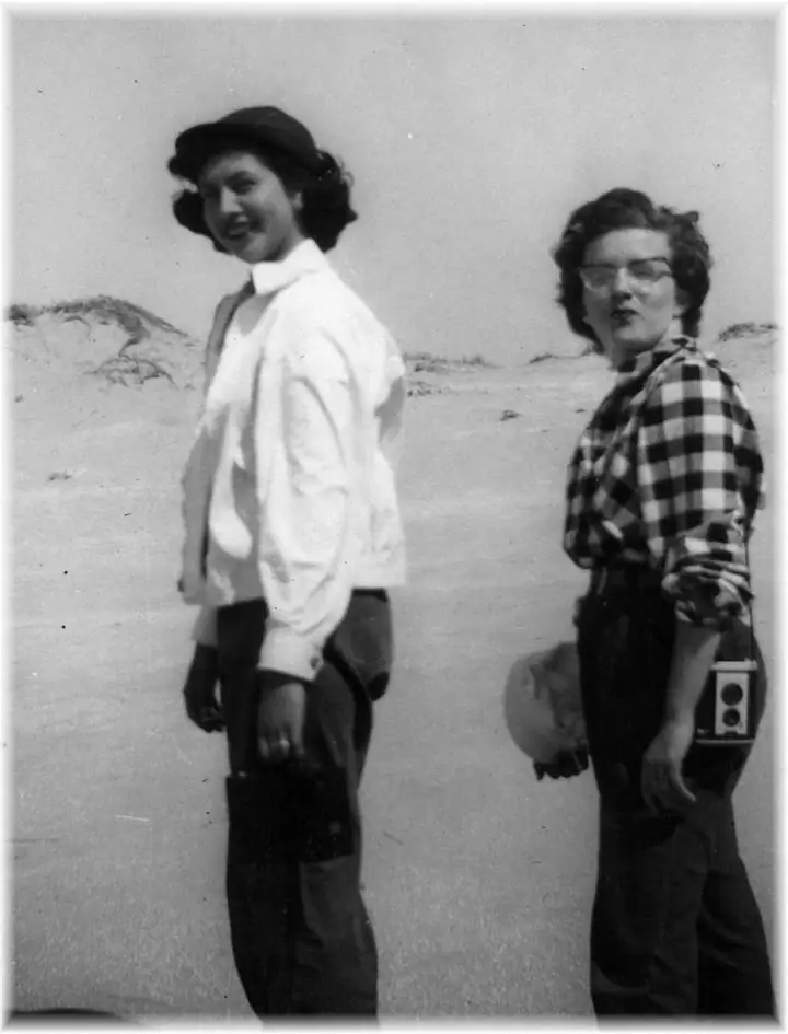 Black-and-white portrait of two women standing among sandy dunes.