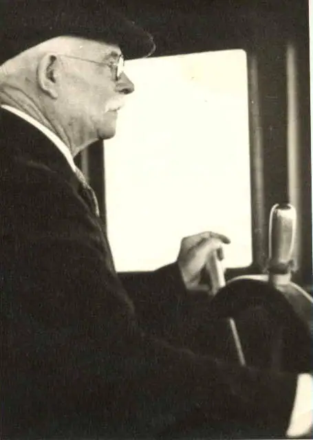 Profile portrait of a hat-wearing man at a steering wheel beside a bright window.