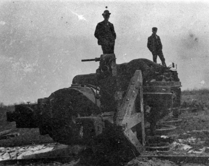 Two men stand on a large piece of heavy machinery in a rough, partly snow-covered field.