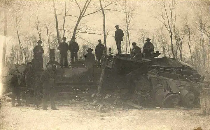 A group of people poses around large logging machinery in a leafless wooded clearing.