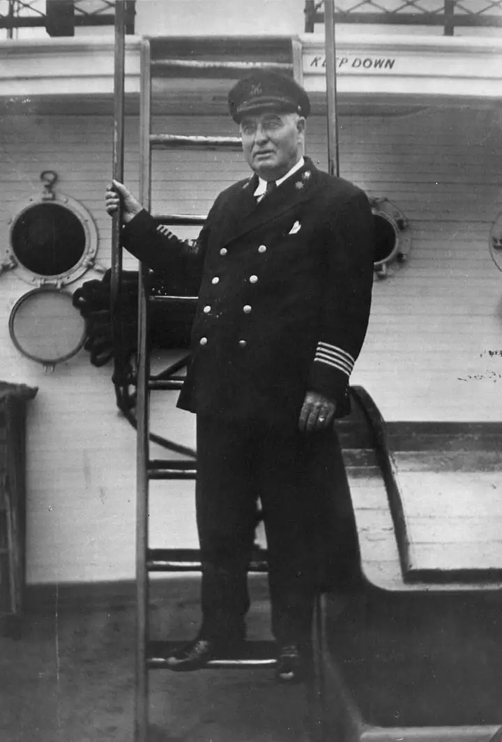 A uniformed man stands beside a ladder on a ship's deck.
