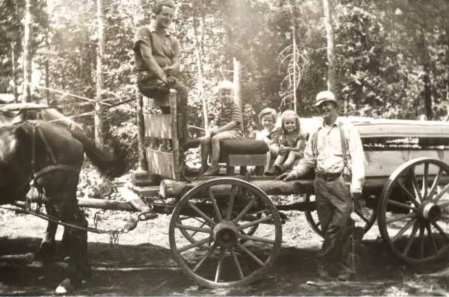 A horse-drawn wagon carries several adults and children through a wooded setting.