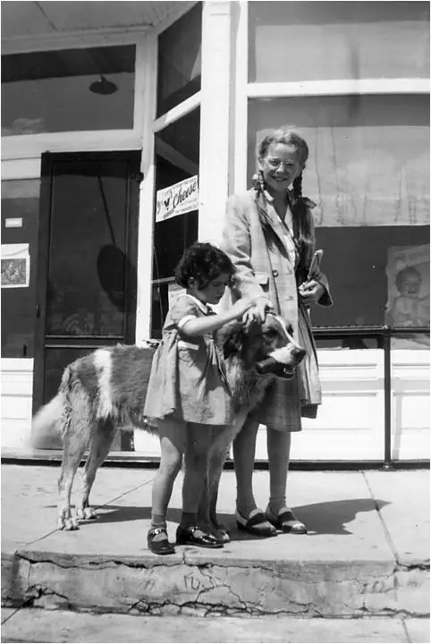 A woman and child stand with a large shaggy dog outside a storefront marked “Cheese.”