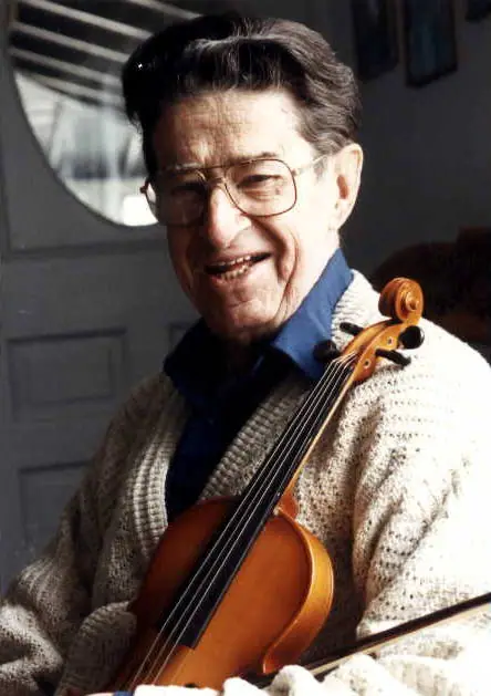 Smiling man in glasses holding a violin and bow indoors.