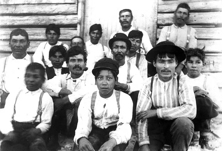 A group of people pose in several rows in front of a log building.