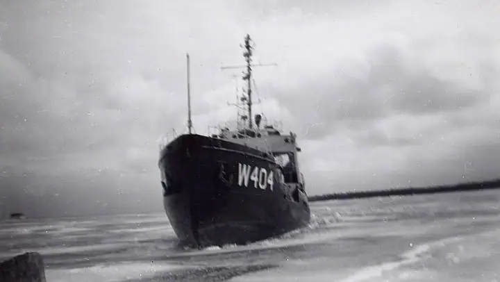A dark vessel marked W404 moves through choppy water beneath a cloudy sky.