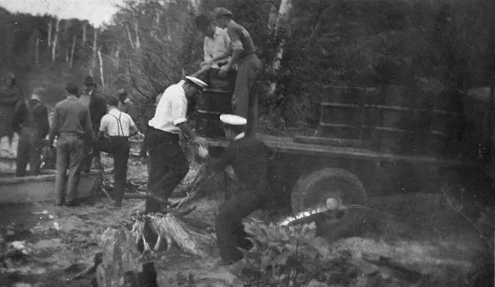 People work beside a truck in a wooded area, handling a large load.