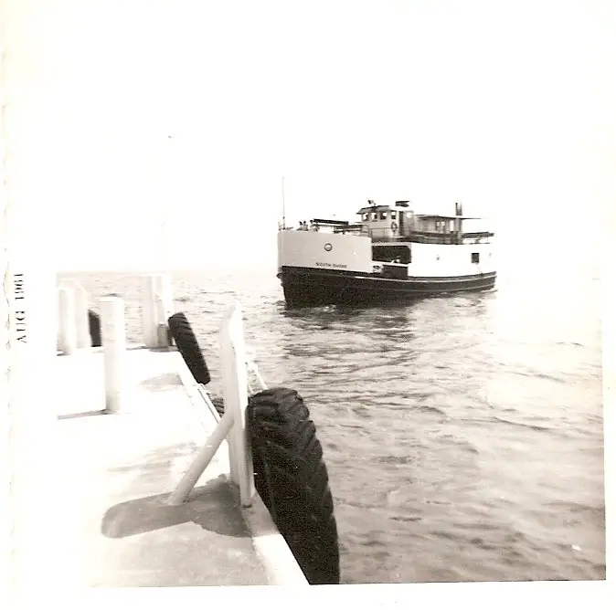 A ferry passes beside a vessel's deck, with large tires along the railing.