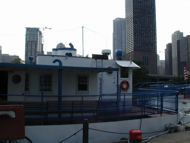 A white-and-blue passenger vessel is moored beside a dock, with high-rise buildings behind it.