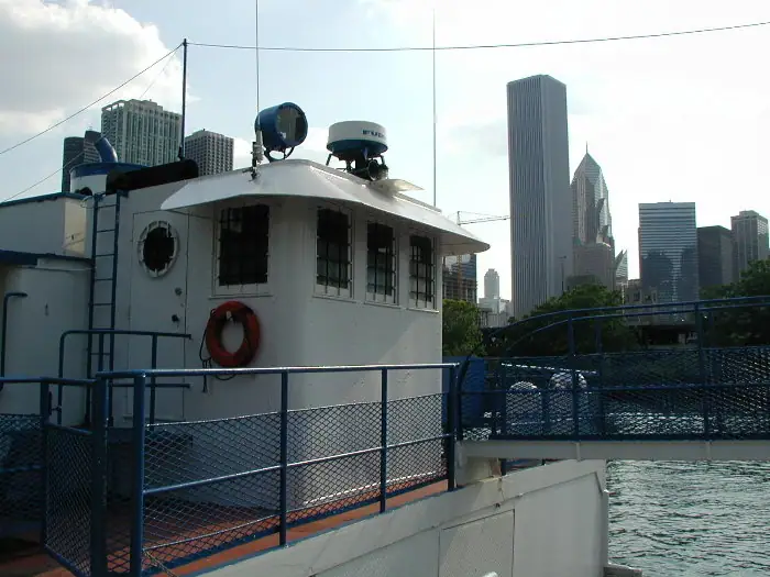 White vessel pilothouse with radar, life ring, railings, and a dense high-rise skyline beyond the water.