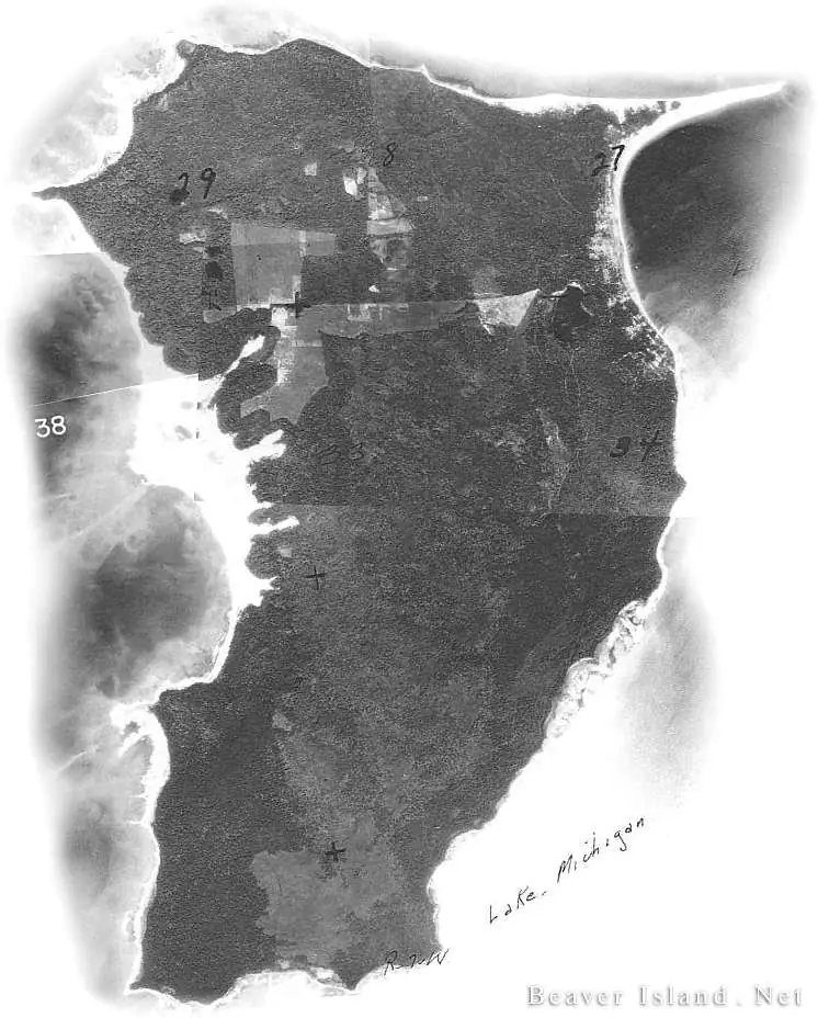 Annotated black-and-white aerial photograph showing a wooded landmass, fields, shorelines, and handwritten markings.
