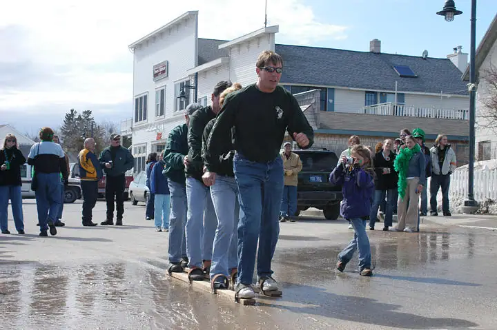 People take part in a team game on wet pavement while spectators watch from the roadside.