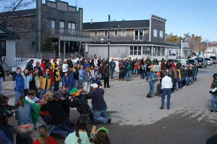 A tug-of-war draws a large crowd on a street outside a building marked HARBOUR MARKET.