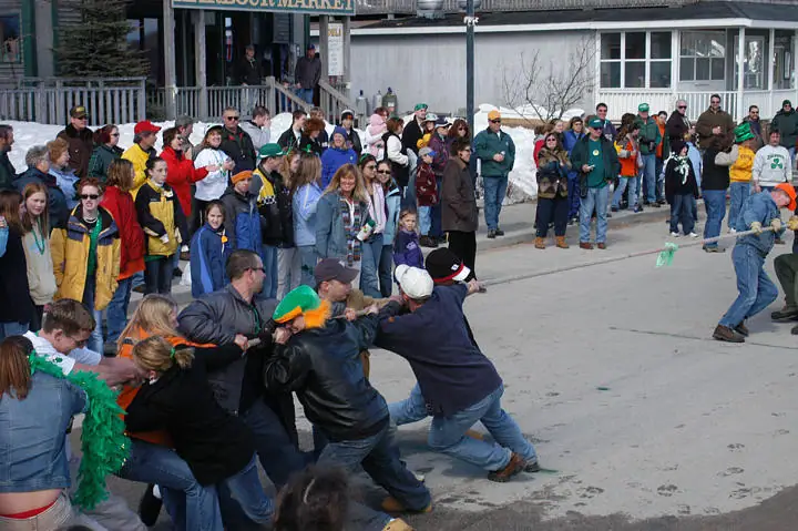 A crowd watches a tug-of-war on a paved street outside a storefront.