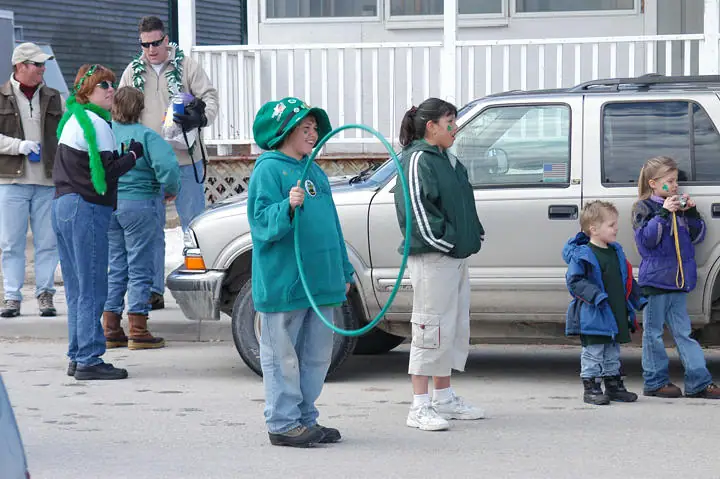 Adults and children gather beside a vehicle, with one child holding a large green hoop.