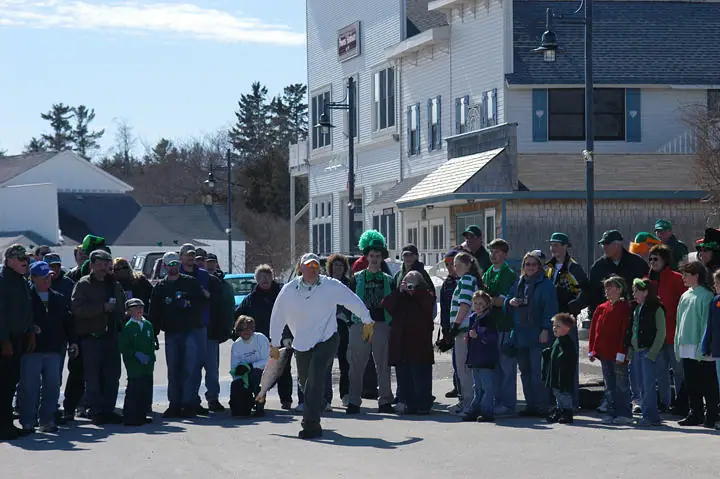 A crowd watches a costumed participant moving along a sunlit street during an outdoor celebration.