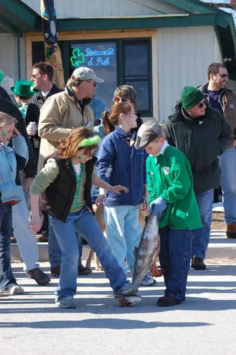 Children and adults gather outside a restaurant while a child holds a large fish.