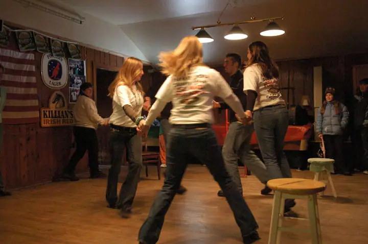 People dance in a wood-paneled room beneath beer signs and an American flag.