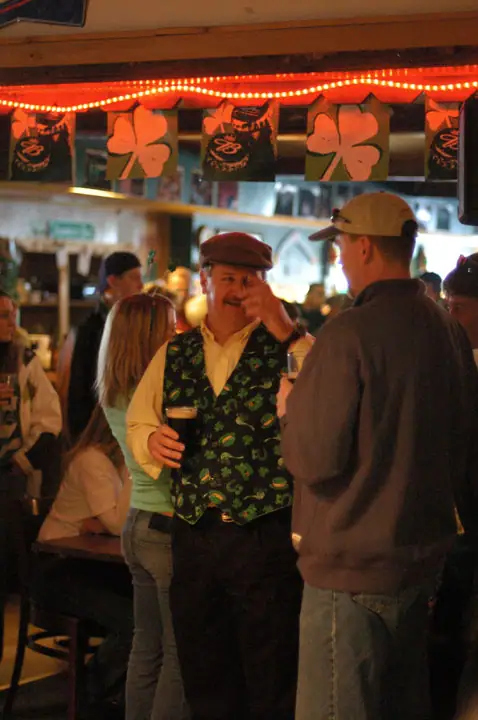 People gather inside a warmly lit bar beneath shamrock decorations.