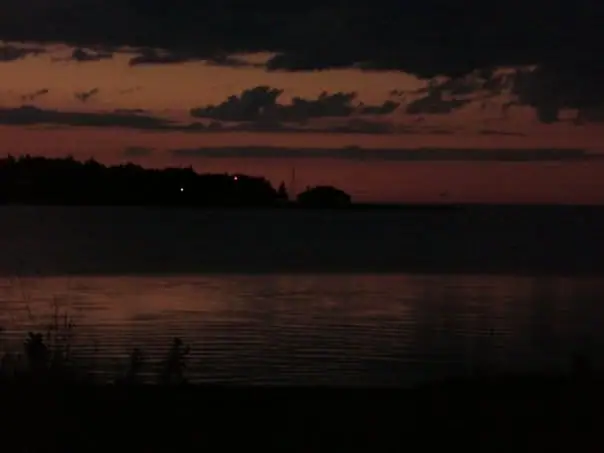 A dark red-orange sky and clouds hang over silhouetted land and calm rippling water.