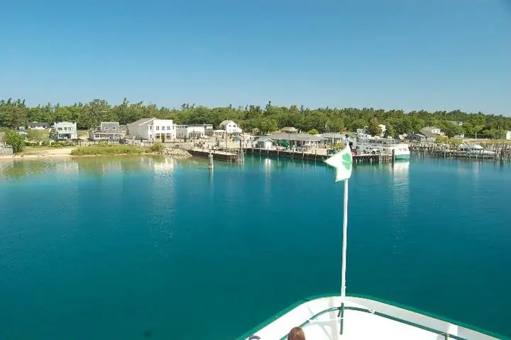 View from a ferry bow toward a tree-lined waterfront with houses, docks, and boats.