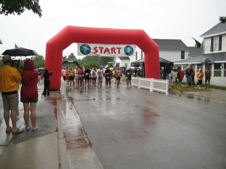 Runners gather beneath a red START arch on a rain-wet street while spectators watch from both sides.