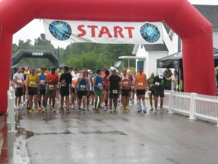 Runners gather beneath a START banner and inflatable arch on a wet paved course.