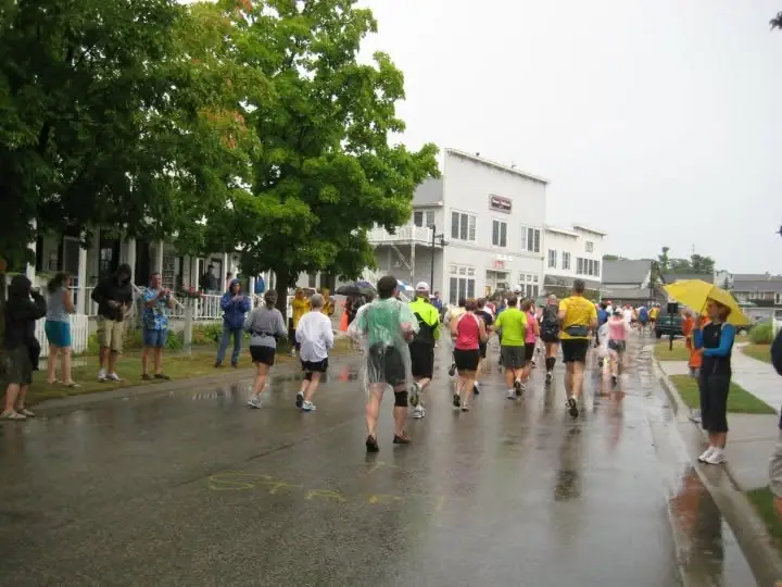 Runners and spectators gather on a wet street beneath umbrellas.