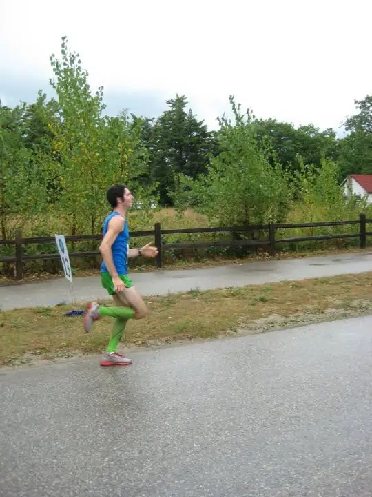 Runner in bright athletic clothing moving along a paved road beside a wooden fence and trees.
