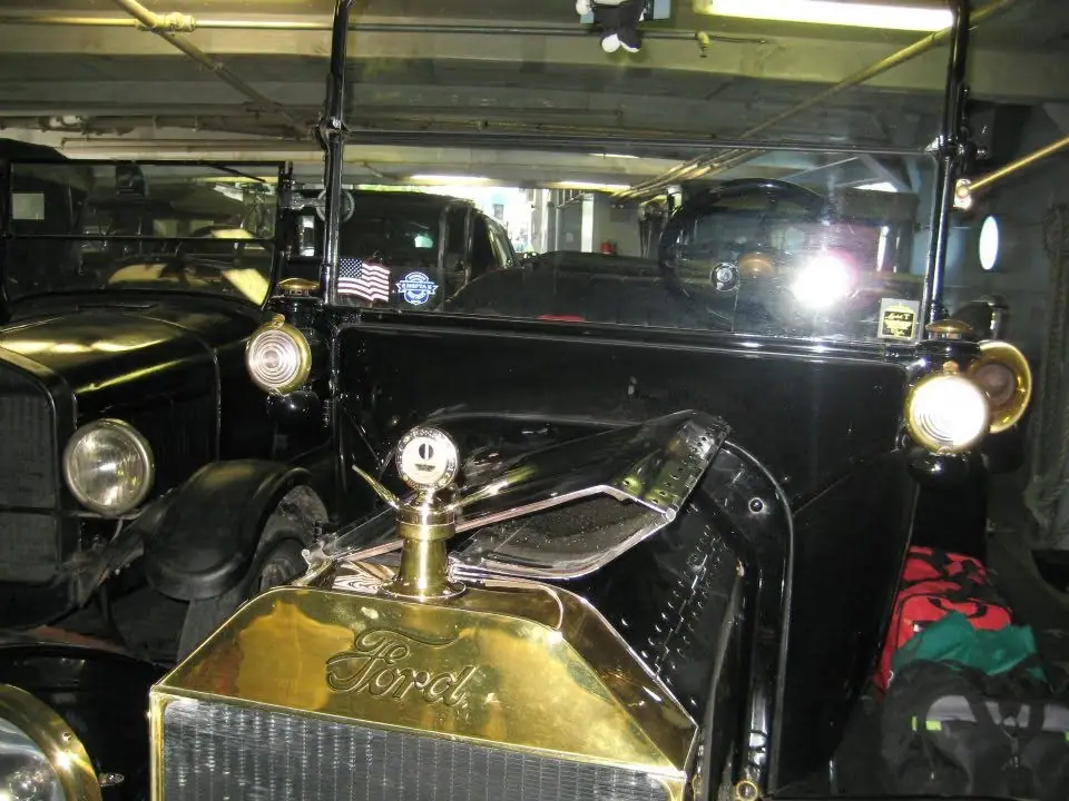 Close view of a black vintage automobile with a brass-colored Ford radiator inside a garage or enclosed vehicle space.