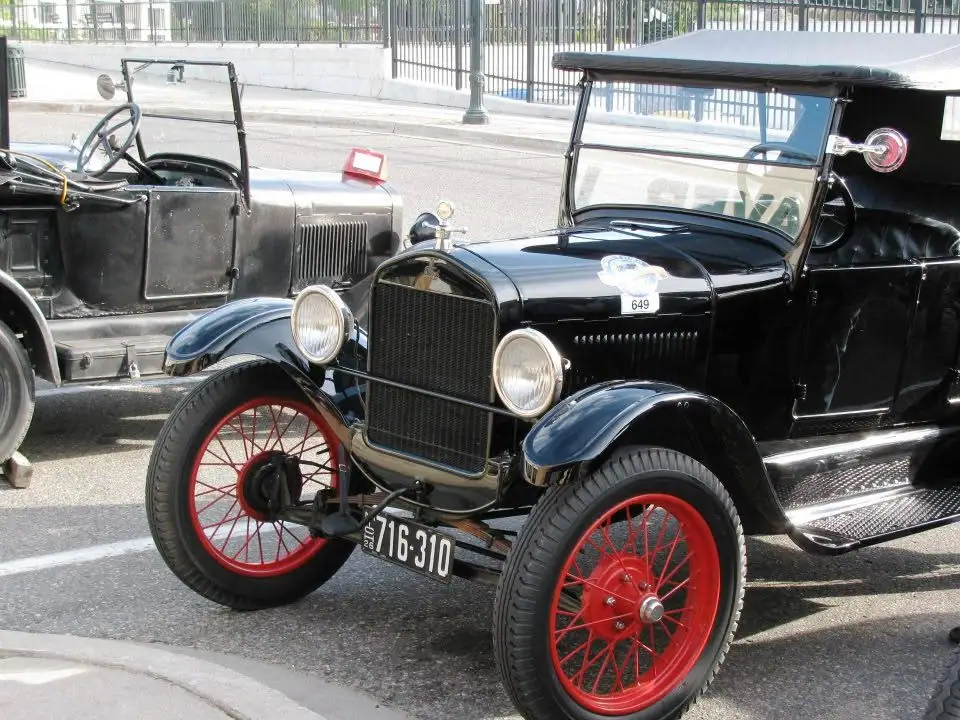 Two black vintage automobiles, including a car with bright red wire wheels, parked along a paved street.