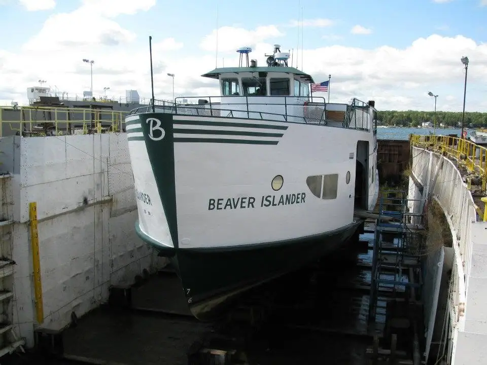 White-and-green ferry BEAVER ISLANDER in a concrete dry dock with an American flag flying from its bridge.