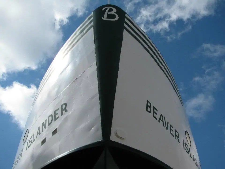 Close-up view of a white ferry bow with black stripes and lettering beneath a partly cloudy sky.