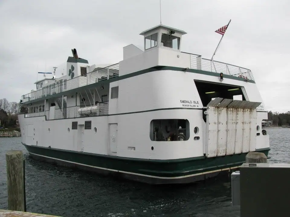 White-and-green ferry moored beside a pier, with an open stern loading door and an American flag.