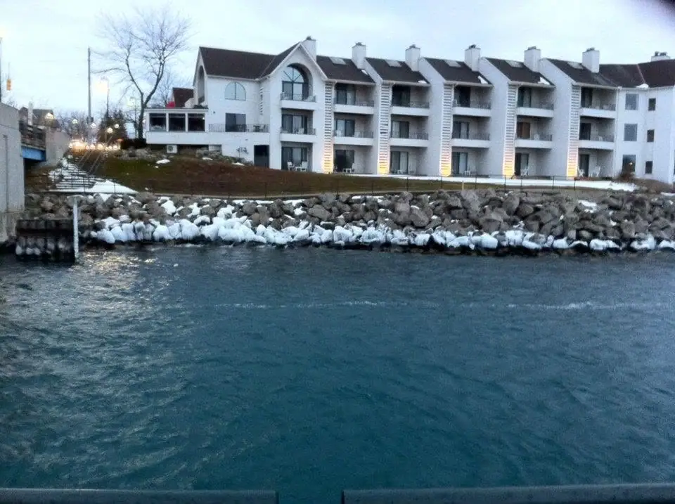 White multi-story waterfront building behind an ice-covered rocky shore and dark rippling water.