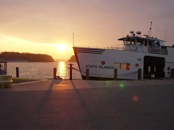 A white ferry is moored beside a pier as the sun sets over the water.