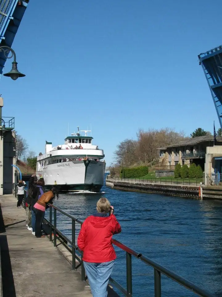 A passenger ferry moves through a raised drawbridge as people watch from a waterfront walkway.