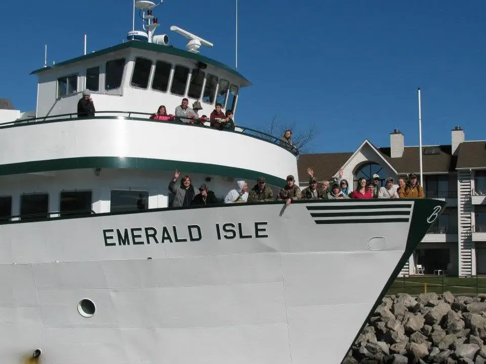 A white passenger ferry with people waving from its decks beside a rocky shore.