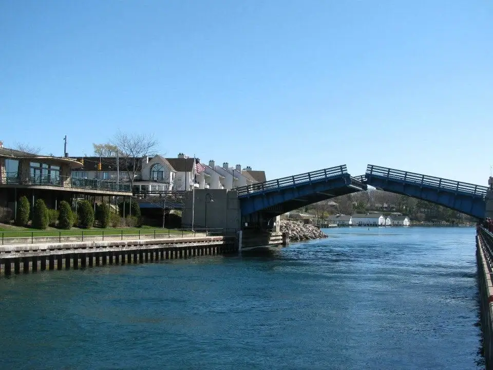 A blue drawbridge stands open over a broad water channel beside waterfront buildings and a pier.