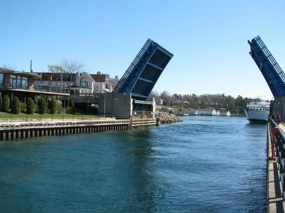 A white ferry passes beneath a raised blue drawbridge along a waterfront.
