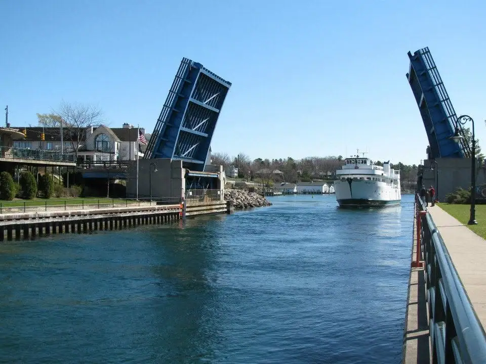 A white passenger ferry approaches between two raised blue drawbridges on a sunny waterfront channel.