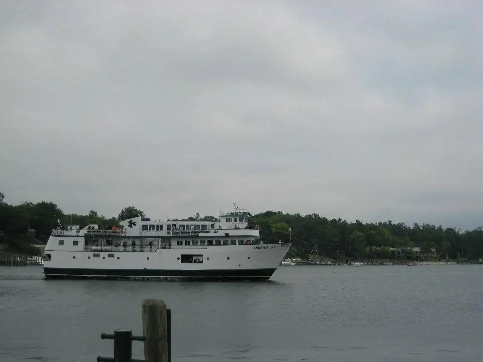 A large white passenger ferry travels across calm water beneath an overcast sky.