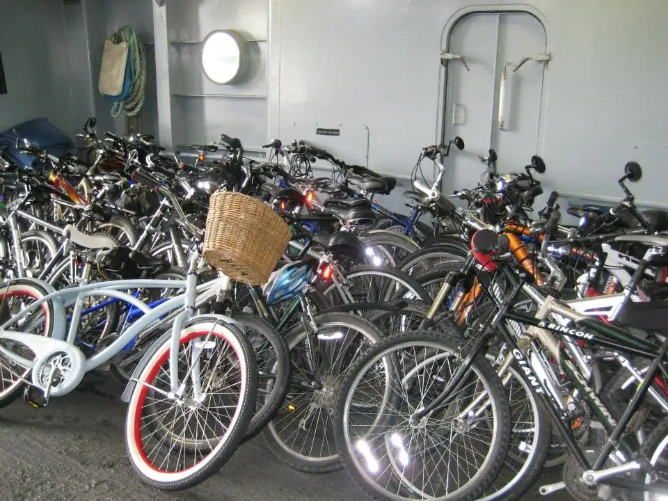 A crowded room holds many bicycles, with a wicker basket prominent in the foreground.