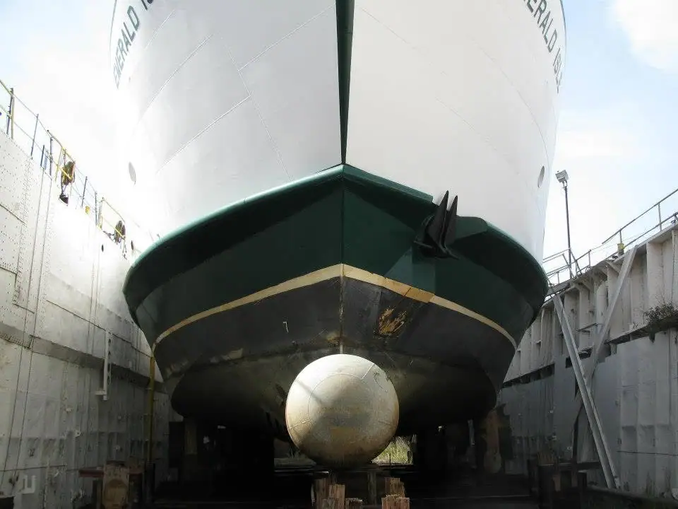 A large white-and-green vessel sits inside a concrete dry dock, viewed from low near its rounded bow.