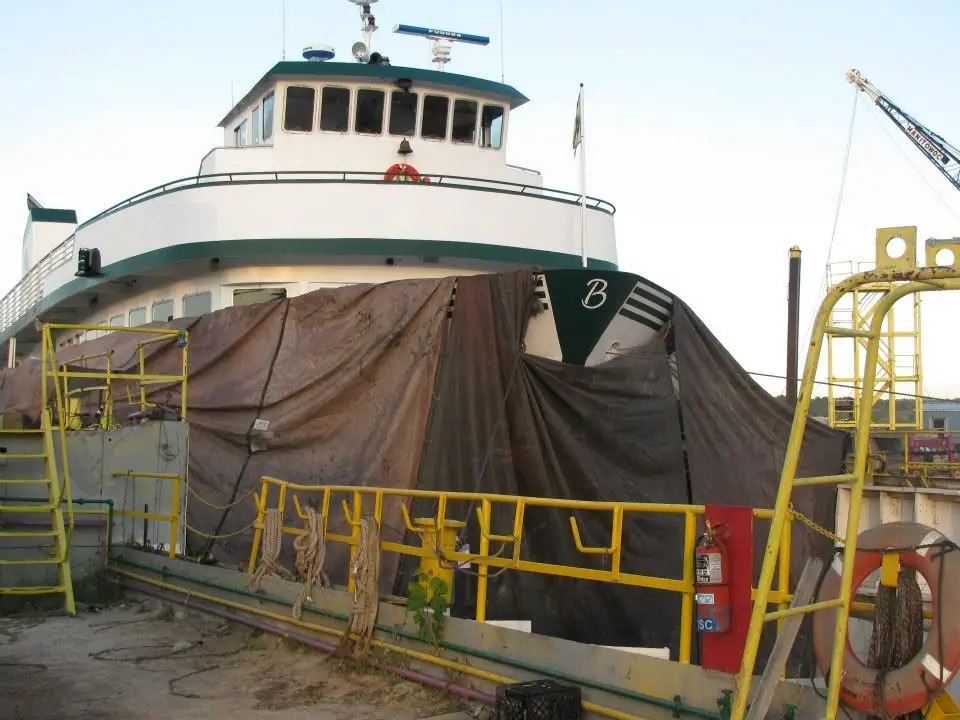 A white ferry with green trim is partly enclosed by a brown covering beside yellow-railed dock equipment.