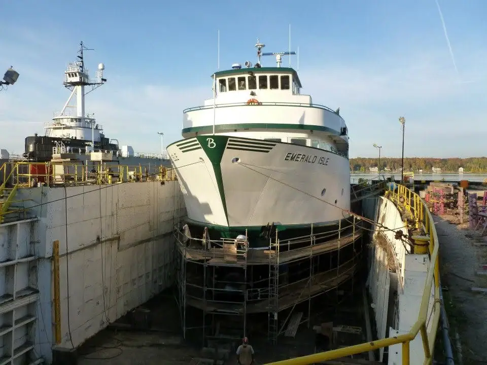 A white ferry sits in a dry dock surrounded by scaffolding and maintenance equipment.