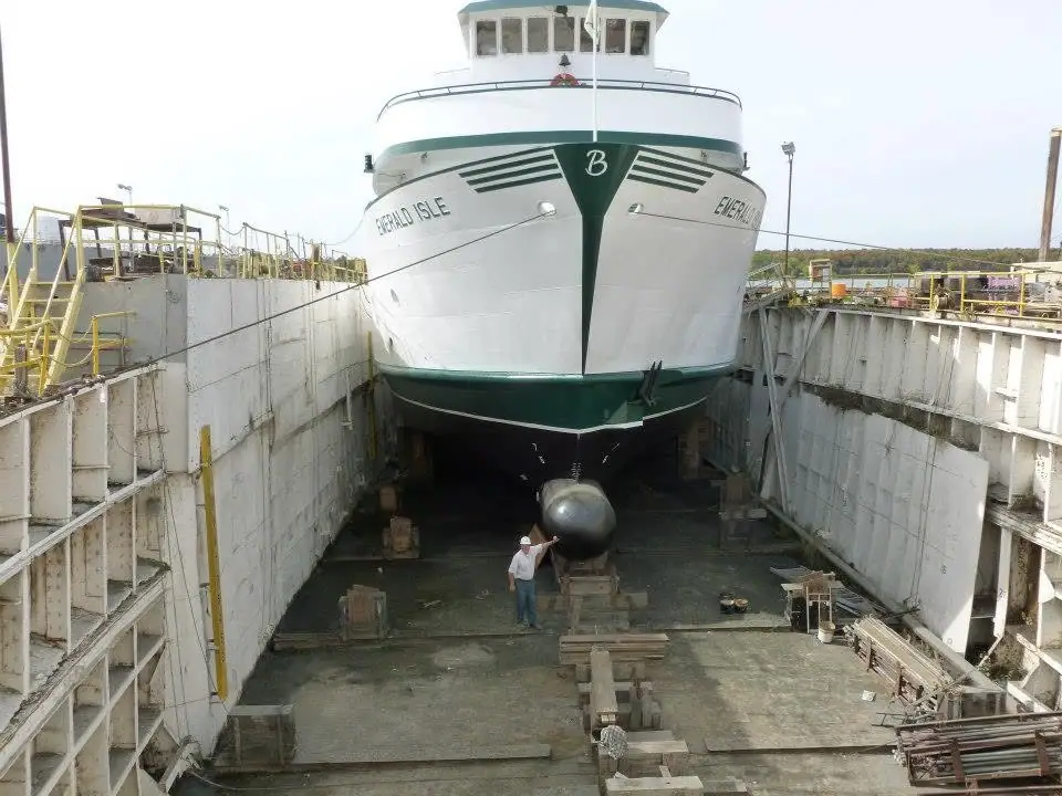 A ferry sits in a dry dock above a worker beside its rounded bow.